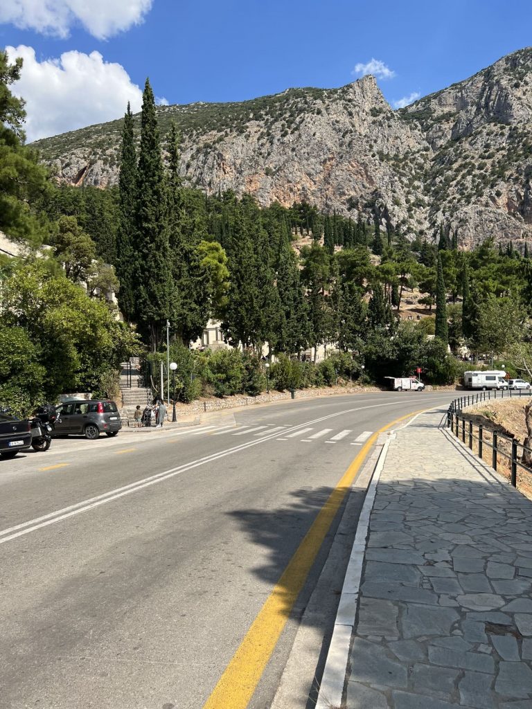 Delphi, Anfahrt zum Heiligtum, Strasse mit Autos, Berg, bewaldet, blauer Himmel, Sonnenschein