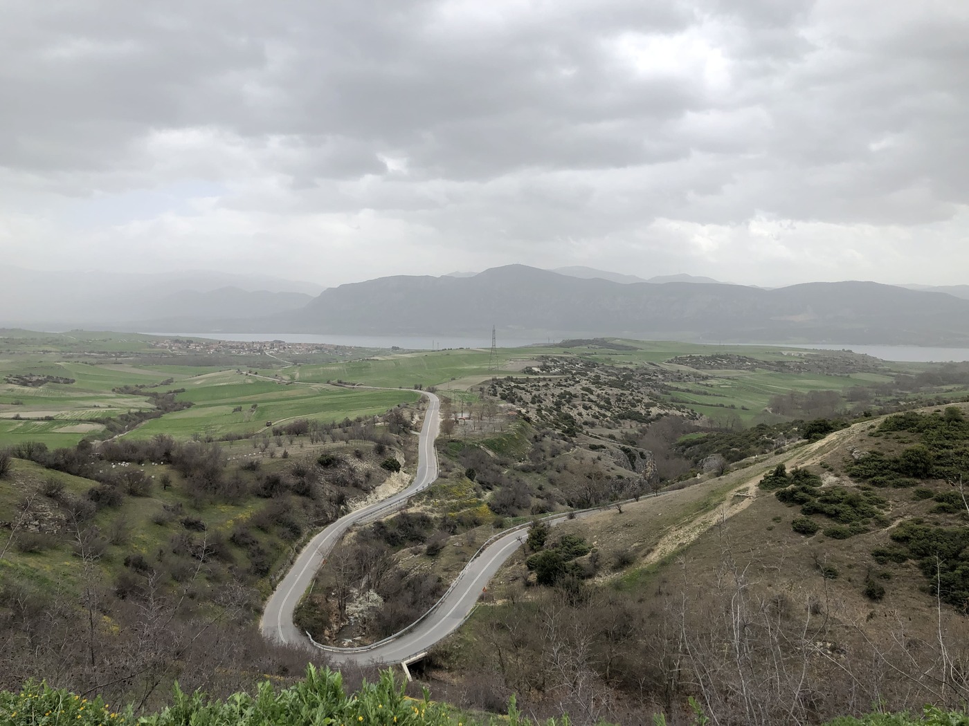 Landschaft mit Strasse, im Hintergrund Berge, Gewässer, grauer Tag, menschenleer